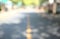 Bokeh asphalt street abstract. Blurry of public community road, downtown path with blurred yellow line, houses, and dim trees.