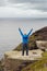 Bold male tourist standing on edge of Cliff of Moher, Ireland, Hands up in the air, back to the viewer