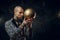 Bold tattooed male model posing for photoshoot in a dark studio and holding a golden soccer ball while looking on it