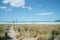 Bollards and rope line sad path to beach and water`s edge under blue sky with few white puffy clouds