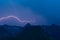 Bolt lightning over mountain peak silhouette with dark blue sky