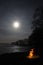 Bonfire flame and moon over lake