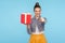Bonus for you, winner! Portrait of optimistic beautiful fashionably dressed girl with hair bun holding gift box and pointing to