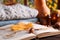 Book with autumn leaf as bookmark, acorns, scented candle and warm sweaters on wooden table, closeup