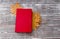 Book of red color, maple leaves on a wooden background.