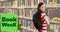 Book week text over portrait of smiling caucasian teenage girl with book standing by bookshelf