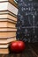 Books and an apple on a wooden table, against the background of a chalkboard with formulas. Teacher's day concept and back to
