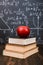 Books and an apple on a wooden table, against the background of a chalkboard with formulas. Teacher& x27;s day concept and back to