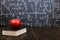Books and an apple on a wooden table, against the background of a chalkboard with formulas. Teacher's day concept and back to