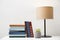 Books, lamp and houseplant on white table near light grey wall