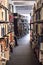 Books on library shelves with leg of person visible further down the isle.  Modern building