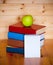 Books, notepad and apple on wooden table over wooden background