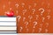 Books on the table against orange blackboard with question marks