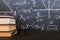 Books on a wooden table, against the background of a chalk board with formulas. Teacher's day concept and back to school