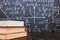 Books on a wooden table, against the background of a chalk board with formulas. Teacher& x27;s day concept and back to school