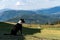 Border collie standing in hilltop yard keeping watch, wood fence, pasture, and cloudy sky and mountains in background