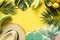 Border of outfit beach female accessories. Tropical vacations, straw sun hat, towel, monstera leaves on yellow. Summer concept