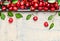 Border of sweet cherries with green leaves on light wooden background, top view, place for text