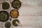 Border of various dried herbs in cups on a light wooden background.