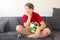 Bored boy sitting on the couch and holding a football ball.