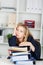 Bored Businesswoman Leaning On Stacked Binders At Desk