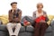 Bored elderly man sitting on a sofa next to an elderly woman knitting