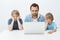 Bored indifferent son sitting with sibling and father at table, leaning head on hands while looking at laptop screen