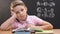 Bored little boy sitting at school desk during math lessons, looking at camera