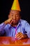 Bored looking man wearing blue shirt and hat sitting by table holding a single candle burning, sad expression facing