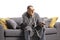 Bored mature man in a bathrobe, sitting on a sofa and holding a tv remote control