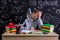 Bored and puzzled youngster sitting at the desk with a head leaned on the hand, writing in the exercise book, surrounded