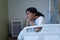 Bored sick mixed race girl sitting on bed in hospital ward holding head in hands