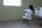 Bored sick mixed race girl sitting on chair in hospital ward looking out of window