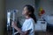 Bored sick mixed race girl standing in hospital ward with iv drip bag on stand looking out of window