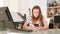 Bored teenage girl sits at a desk and surfs the internet on her smartphone