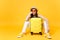 Bored tourist woman in summer casual clothes hat sit with suitcase, wait for plane on yellow orange background