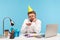 Bored unhappy man office worker in eyeglasses and cone hat looking at cake with candle, lonely celebrating birthday sitting at