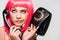 Bored woman in pink wig holding retro telephone, isolated on grey