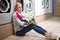 Bored young woman holding dirty clothes and detergent pink bottle in basin