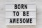 `Born to be awesome` words on a lightbox on a white wooden background, top view. Overhead, from above, flat lay. Close-up