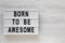 `Born to be awesome` words on a lightbox on a white wooden background, top view. Overhead, from above, flat lay. Copy space