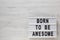 `Born to be awesome` words on a lightbox on a white wooden surface, top view. Overhead, from above, flat lay. Copy space
