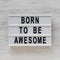 `Born to be awesome` words on a modern board on a white wooden background, top view. Overhead, from above, flat lay