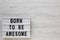 `Born to be awesome` words on a modern board on a white wooden surface, top view. Overhead, from above, flat lay. Copy space