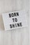 `Born to shine` words on a lightbox on a white wooden background, top view. Overhead, from above, flat lay. Closeup