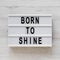 `Born to shine` words on a lightbox on a white wooden surface, top view. Overhead, from above, flat lay. Close-up