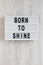 `Born to shine` words on a modern board on a white wooden background, top view. Overhead, from above, flat lay. Close-up