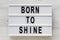 `Born to shine` words on a modern board on a white wooden surface, top view. Overhead, from above, flat lay. Close-up