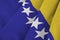 Bosnia and Herzegovina flag with big folds waving close up under the studio light indoors. The official symbols and