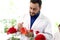 Botanist scientist in hold chemical extraction glass flask standing near red rose flower, biological researcher man do science